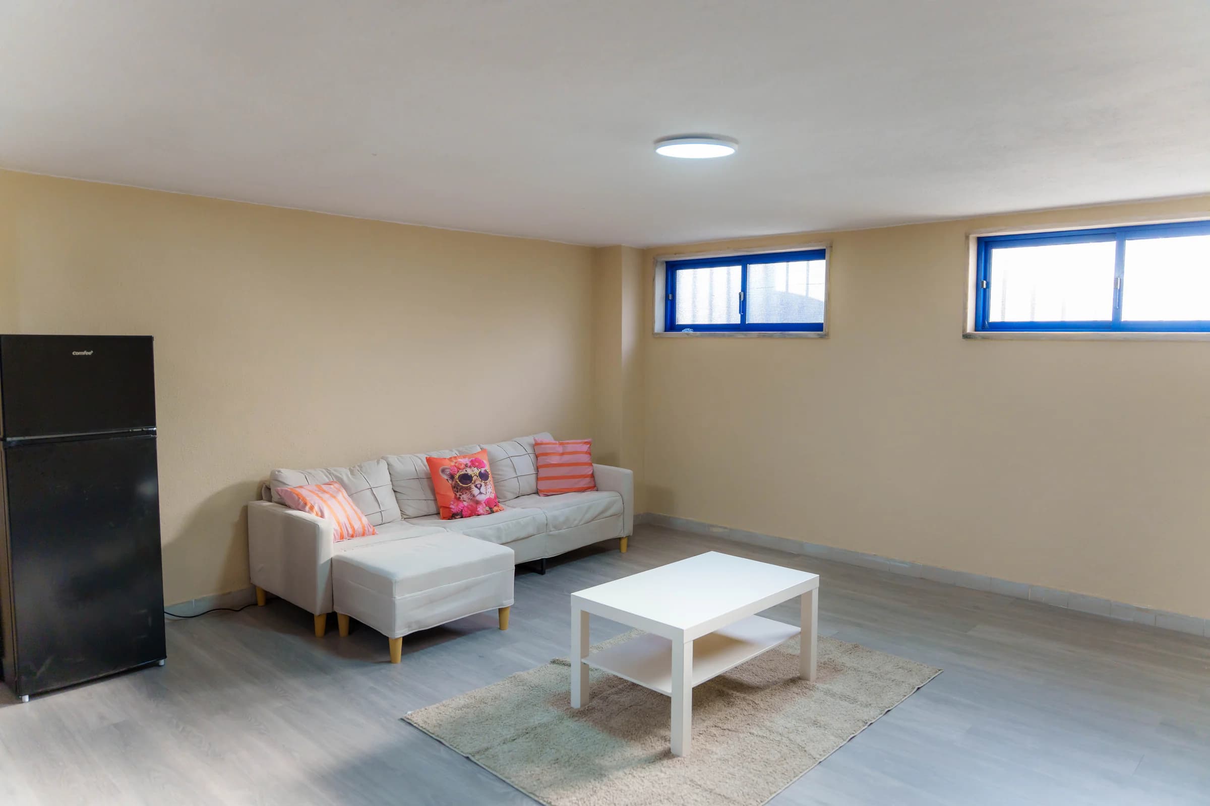 Sala privada de festas com sofá de canto, mesa branca e frigorífico