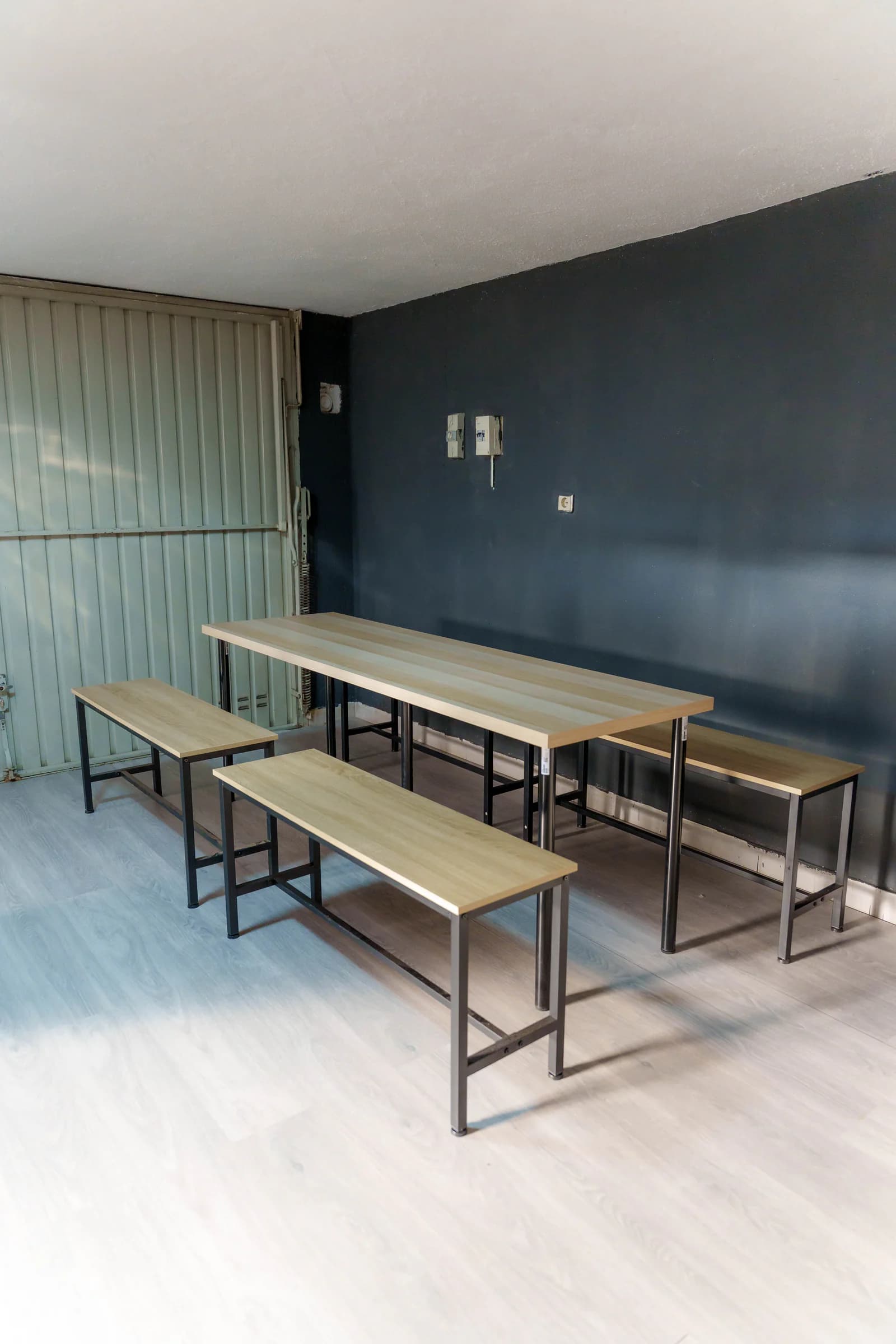 Mesa comprida com bancos de madeira encostada à parede escura da sala de festas