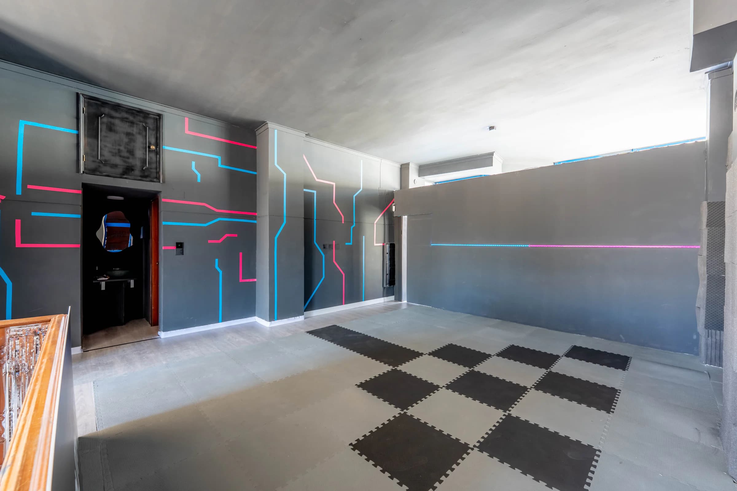 Arena vazia vista de um canto, com uma fita de luz azul e rosa a atravessar a parede